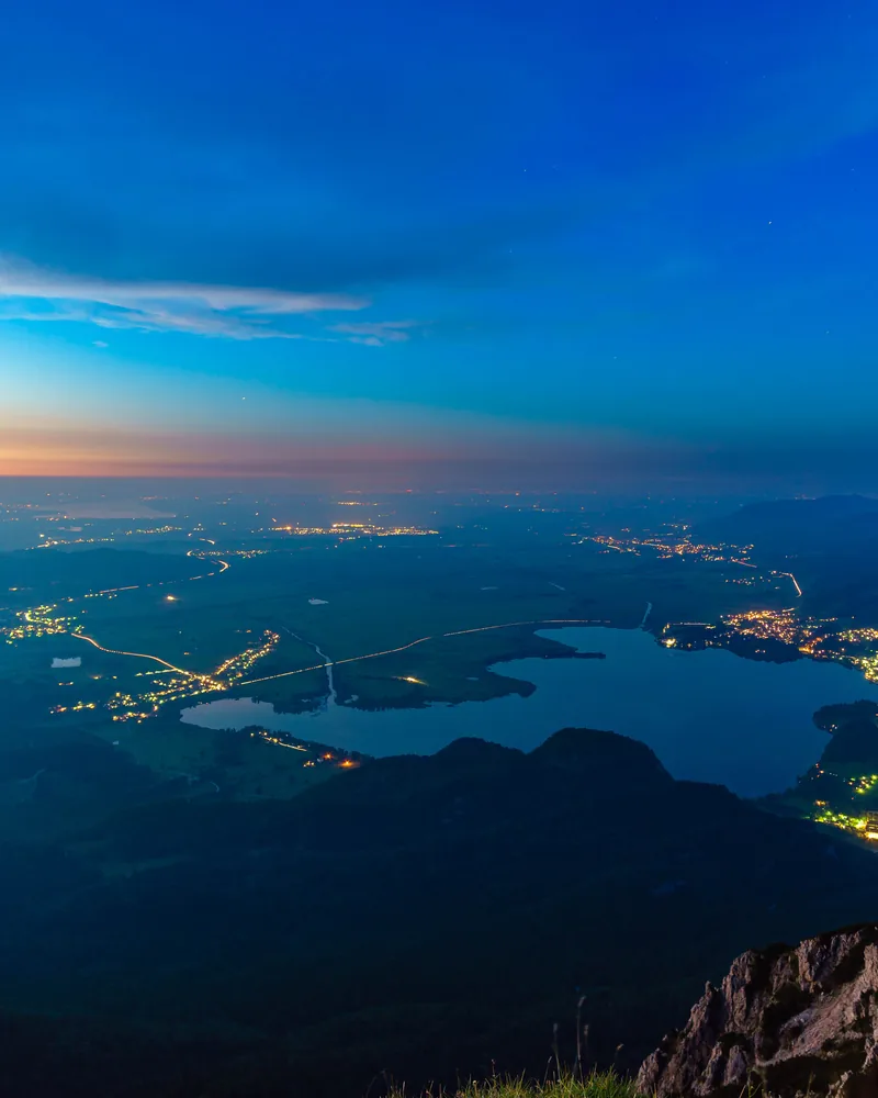 View from a mountain over a lake and lit-up towns at blue hour